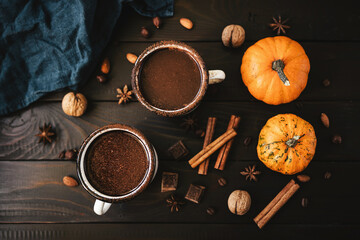 Top view of two mugs of hot chocolate, pumpkins and spices on rustic wooden background, cozy autumn scene