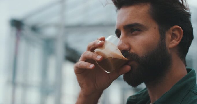 Young handsome man drinking coffee outdoors with transparent cabins in background, close-up