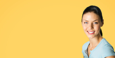 Portrait image of young happy smiling cute brunette woman wear blue casual clothing, posing at studio, isolate yellow color background, with free space blank text area