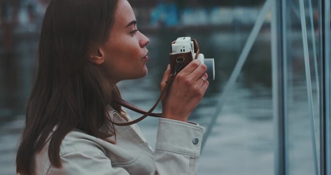 Beautiful young woman inside glass cabin framing shot with instant camera
