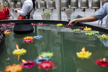 Person reverently places vibrant floating candle into tranquil pool, surrounded by illuminated colorful lotus blossoms. peaceful cultural ceremony temple evokes spiritual devotion and serenity