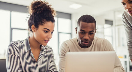 Three young African American colleagues collaborate on a laptop, showcasing teamwork and focused problem-solving in a modern office setting