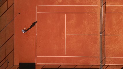 Aerial view of a tennis player practicing on a clay court, highlighting focused training and athleticism. The vibrant red surface underscores dedication to skill development in sports education.