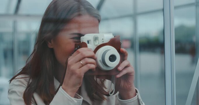 Beautiful young woman inside glass cabin taking instant photo with film coming out of camera
