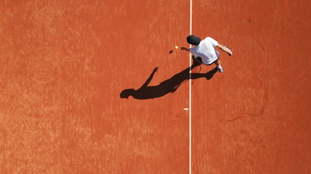 Tennis player practices on clay court, showcasing dynamic movement and skill development. Overhead drone footage highlights focused training, dedication, and precision in sports education.