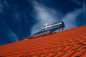 Solar water heater boiler on rooftop , dark blue sky with white washed clouds.