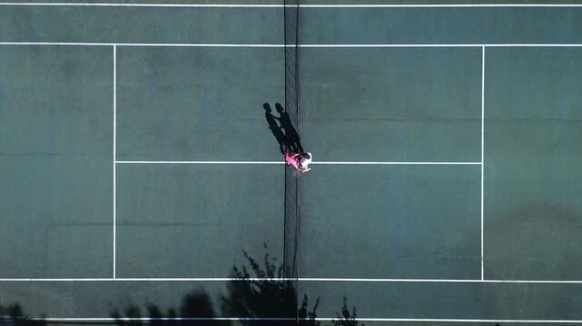 Two athletes practice doubles tennis on a hardcourt, showcasing dynamic positioning and teamwork from an aerial view, emphasizing skill development in sports training.