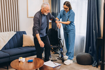 Nurse assisting senior man standing up from wheelchair