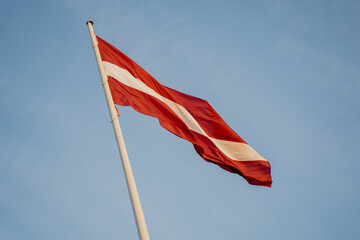 Latvian national flag waving on tall flagpole against clear blue sky representing state identity, national pride, independence and official government symbolism