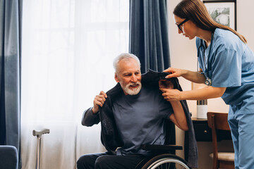 Caregiver helping senior man getting dressed