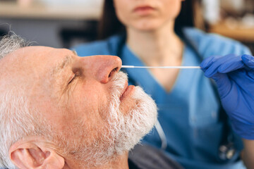 Senior man receiving nasal swab covid test from nurse