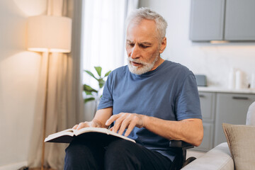 Senior man in wheelchair reading book at home