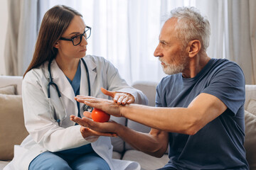Doctor assisting senior man with hand exercise using therapy ball