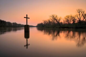 Cross in water at sunset with reflection and trees in the background at dusk light sky