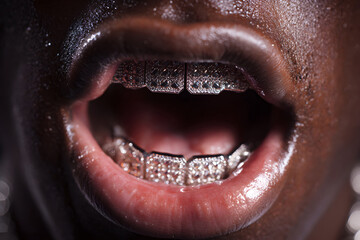 Close up of a black man&rsquo;s mouth open with shiny diamond grillz on teeth and glossy lips with wet skin texture