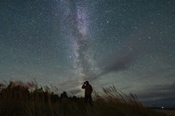 Awe-inspired silhouette of a man stargazing at the vibrant Milky Way galaxy and countless stars in the dark night sky. © Dmitri