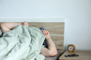 Man burrows under the blanket, trying to escape the new day, symbolizing the challenge of early...