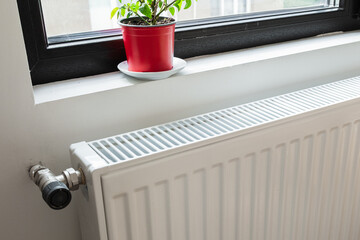 A white heat radiator is installed beneath a window. The fall of the cold weather and the rise in...