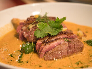 Seared Duck Breast in Orange Sauce - A close-up, appetizing view of a perfectly cooked duck breast sliced and served in a creamy, vibrant orange sauce, garnished with herbs.