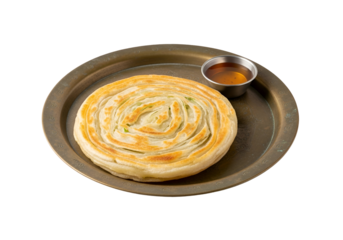 A golden-brown, spiral-shaped flatbread sits on a dark metal tray, accompanied by a small bowl of honey.