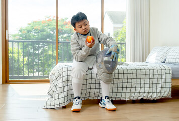 Asian boy with fencing sport uniform sit on bed and enjoy to eat an apple and relax after practice in bedroom.