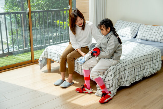 Asian mother sit near her child and help to wear uniform of fencing sport in bedroom with soft morning light and happiness. - Powered by Adobe