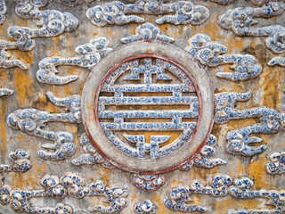 Detailed ceramic wall with intricate Asian motifs - Close-up shot of a textured wall with ornate blue and white porcelain tiles and a central circular relief.