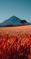A vibrant vista of a mountain landscape, a solitary tree standing amidst a field of ripened, fiery-red wheat.