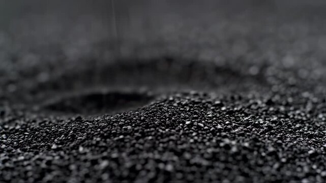 Close-up of black chia seeds falling and forming a small pile on a dark surface.