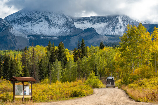 Fototapeta Camper van on dirt road with beautiful fall foliage scenery of snowcapped Rocky mountain, yellow aspen and pine trees in Gunnison National Forest near Crested Butte, Colorado, USA.