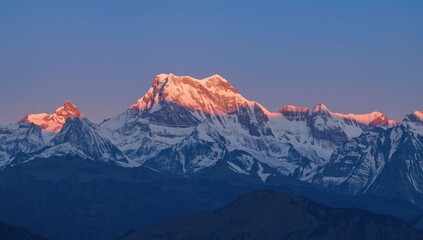 Fototapeta premium Majestic snow-covered mountain range is illuminated by the warm golden light of sunrise, creating a stunning and vibrant display of nature's beauty against a clear blue sky.