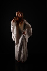 Low key full length portrait of beautiful ginger young woman in vintage white dress