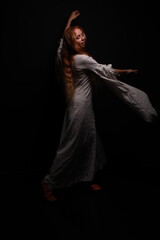 Full length portrait of a young red-haired woman in a vintage white dress in a low key