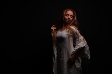 Low key portrait of a young red-haired woman in a vintage white dress in shadows