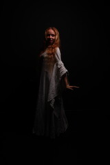 Full length portrait of a young red-haired woman in a vintage white dress in a low key