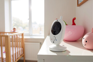 Modern baby monitor camera on a shelf providing video surveillance and safety for a child sleeping in a crib in a bright nursery
