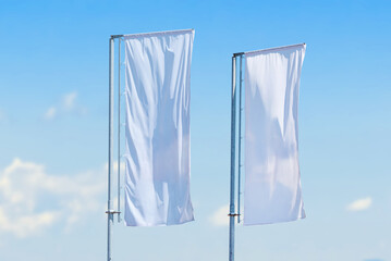 Two tall vertical white flags waving on metal poles against clear blue sky, minimalistic outdoor advertising concept