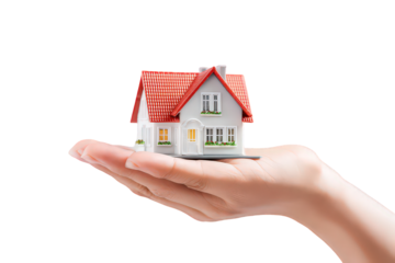 Hand Holding a Small White House Model with Red Roof Against a Black Background