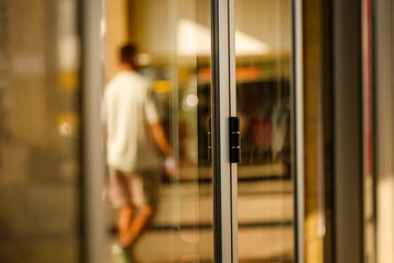 Blurred reflection of a man on glass doorway of a public building, abstract urban detail with distorted silhouette, symbolizing identity, citizenship, and social belonging.