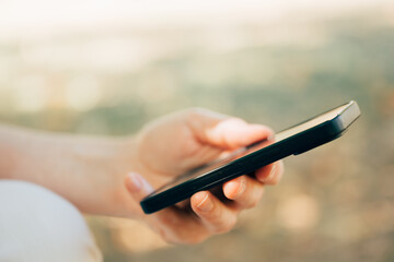 Closeup of female hand holding smartphone in park on a sunny summer day, symbolizing technology, connection, and lifestyle.