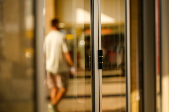 Blurred reflection of a man on glass doorway of a public building, abstract urban detail with distorted silhouette, symbolizing identity, citizenship, and social belonging.