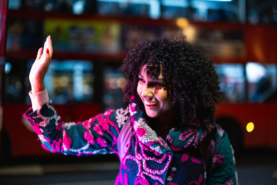 Smiling woman waving hand at night city bus
