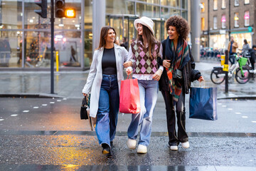 Women friends crossing street carrying shopping bags
