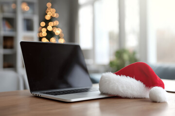 Fototapeta premium Laptop on table with Christmas hat and festive decor in background