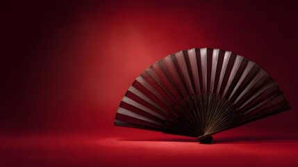 A traditional wooden folding fan rests on a vibrant red surface with a soft gradient background
