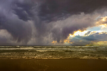 Dramatic seascape with dark storm clouds over the North Sea, strong waves crashing onto the sandy shore, and a moody horizon.