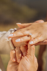 Close-up of a man's hand putting a wedding ring on a woman's finger, mountain scenery, engagement concept.