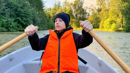 Teen Boy Rowing Boat In Bright Orange Vest On Calm Forest Lake At Sunset. Concept Of Outdoor Adventure, Autumn Travel, Youth Healthy Activities, And Nature Getaways For Eco Lifestyle Visuals