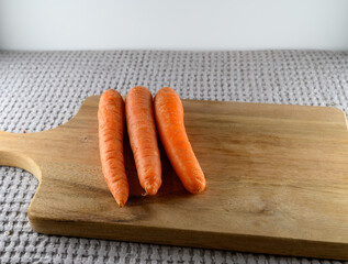 Three fresh orange carrots sit neatly on a wooden cutting board. The soft texture of the board contrasts with the vibrant color of the carrots, ideal for a healthy meal
