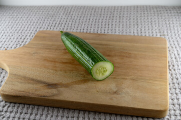 A freshly cut cucumber rests on a wooden cutting board in a bright kitchen. The vibrant green skin and crisp texture highlight the freshness of the vegetable